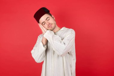 Kırmızı arka planda poz veren fes takan yakışıklı bir genç.