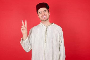 Kırmızı arka planda poz veren fes takan yakışıklı bir genç.