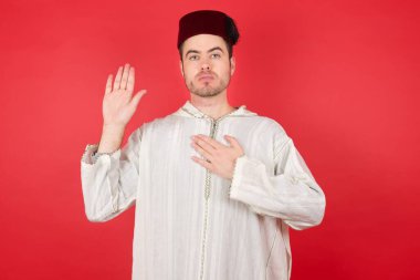Kırmızı arka planda poz veren fes takan yakışıklı bir genç.