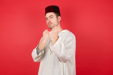 Kırmızı arka planda poz veren fes takan yakışıklı bir genç.