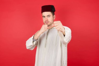 Kırmızı arka planda poz veren fes takan yakışıklı bir genç.