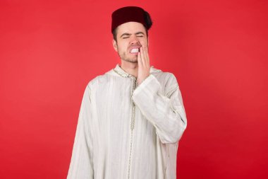 Kırmızı arka planda poz veren fes takan yakışıklı bir genç.