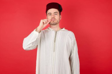 Kırmızı arka planda poz veren fes takan yakışıklı bir genç.