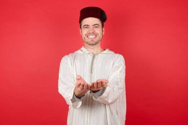 Geleneksel Türk şapkası takan yakışıklı genç bir adam avuç içi fes takıyor ya da el hareketi yapıyor. Tutun ve koruyun