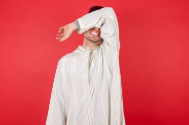 Geleneksel Türk şapkası takan yakışıklı genç adam Fez kollarıyla gözlerini kapatıyor neşeli ve komik gülümsüyor.