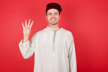 Geleneksel Türk şapkası giyen yakışıklı genç adam dört numaralı parmaklarıyla kendini beğenmiş ve mutlu gülümserken görülüyor..