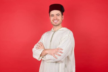 Geleneksel Türk şapkası giyen, kollarını kavuşturup kameraya bakan yakışıklı genç adam. Pozitif kişi.