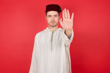 Geleneksel Türk şapkası giyen yakışıklı genç adam uyarı ifadesiyle fes, sarı arka planda izole edilmiş yüzünde negatif ve ciddi bir jest..