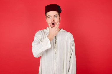 Geleneksel Türk şapkası takan yakışıklı genç adam inançsızlıktan, şaşkınlıktan ve elleri çenesinde olan şaşkınlıktan büyülenmiş görünüyor.