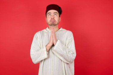 Geleneksel Türk şapkası takan yakışıklı genç adam elleri ile dua ederken yüzünde umut ifadesi var. Çok duygusal ve endişeli. Soruyorum.