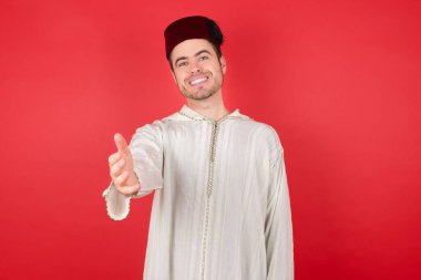 Geleneksel Türk şapkası fes takan yakışıklı genç adam dostça gülümsüyor ve selamlama ve hoş geldin demek için tokalaşıyor. Başarılı bir iş..