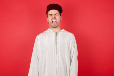 Geleneksel Türk şapkası takan yakışıklı genç adam komik bir ifadeyle dilini dışarı çıkartıyor. Duygu kavramı.