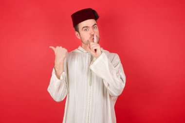 Geleneksel Türk şapkası takan yakışıklı genç adam sessiz olmak istiyor. Parmakları dudaklarında, elleri yanda. Sessizlik ve gizli konsept.