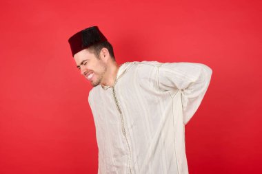 Geleneksel Türk şapkası takan yakışıklı genç adam sırt ağrısı çekiyor, elleriyle dokunuyor, kas ağrısı çekiyor.