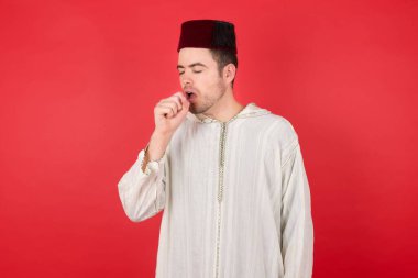 Geleneksel Türk şapkası takan yakışıklı genç adam kendini kötü hissediyor ve soğuk algınlığı veya bronşitin belirtisi olarak öksürüyor. Sağlık hizmetleri kavramı.