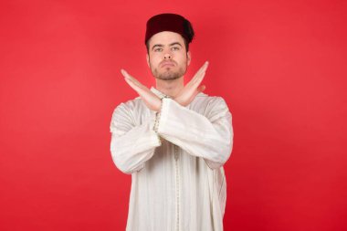 Geleneksel Türk şapkası giyen yakışıklı genç adam Fez kollarını kavuşturuyor, negatif işaret veriyor, kızgın surat yapıyor.