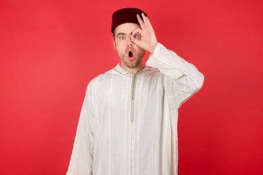 Geleneksel Türk şapkası takan yakışıklı genç adam şaşırmış yüz ifadesiyle şaşırmış, parmaklarından bakan bir jest yapıyor. İnançsız ifade.