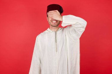 Geleneksel Türk şapkası takan yakışıklı bir genç adam. Gülümsüyor ve elleri yüzünde, şaşırmak için gözleri kapatıyordu. Kör kavram.