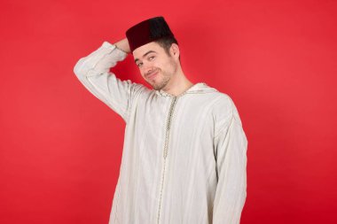 Geleneksel Türk şapkası giyen yakışıklı genç adam Fez 'in kafası karışmış ve bir şeyi merak ediyor. Elini başının üstünde tutuyor, şüpheyle emin değil. Düşünceli kavram.