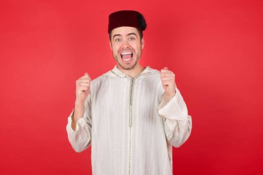 Geleneksel Türk şapkası giyen yakışıklı genç adam fez, kollarını kaldırıp gözlerini açarak başarının şaşkınlığını ve şaşkınlığını yaşadı. Kazanan konsept.