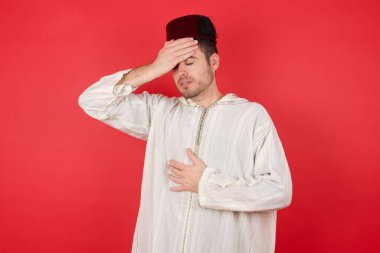 Geleneksel Türk şapkası takan yakışıklı genç adam hastalık, ateş, grip ve soğuk algınlığı için alnına dokunuyor..