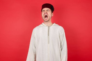 Geleneksel Türk şapkası takan yakışıklı genç adam öfkeli ve öfkeli çığlıklar atıyor, öfkeyle bağırıyor. Öfke ve agresif kavram.
