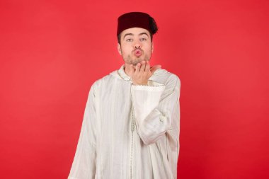 Geleneksel Türk şapkası takan yakışıklı genç adam kameraya bakıyor ve havada el ele öpüşüyor. Güzel ve seksi. Aşk ifadesi.