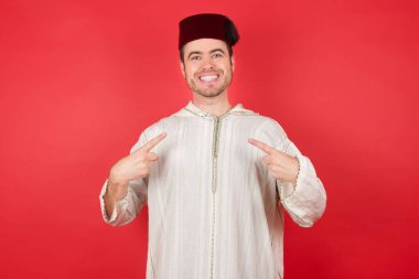 Kırmızı arka planda poz veren fes takan yakışıklı bir genç.