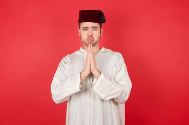 Kırmızı arka planda poz veren fes takan yakışıklı bir genç.