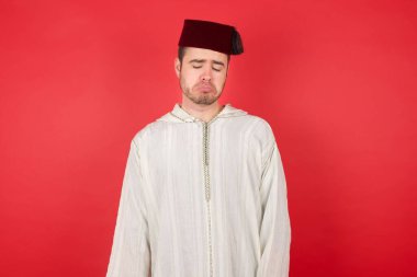 Kırmızı arka planda poz veren fes takan yakışıklı bir genç.