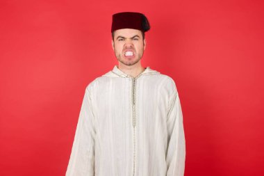 Kırmızı arka planda poz veren fes takan yakışıklı bir genç.