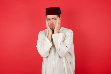 Kırmızı arka planda poz veren fes takan yakışıklı bir genç.