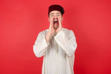 Kırmızı arka planda poz veren fes takan yakışıklı bir genç.