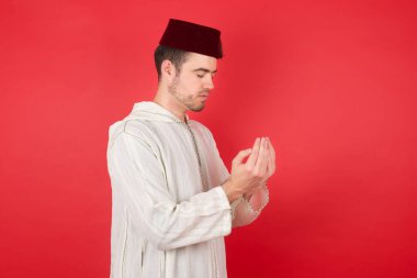 Kırmızı stüdyo arka planında poz veren, fes takan yakışıklı genç bir adam portresi.