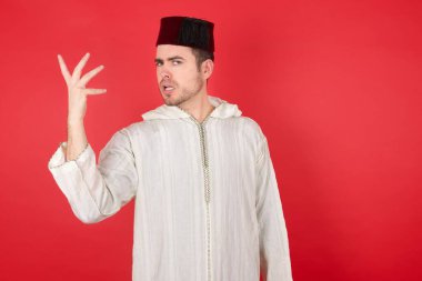 Kırmızı stüdyo arka planında poz veren, fes takan yakışıklı genç bir adam portresi.