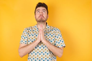 Yakışıklı genç adam elleri ile birlikte dua ediyor. Yüzünde umut ifadesi var. Duygusal ve endişeli. Soruyorum.