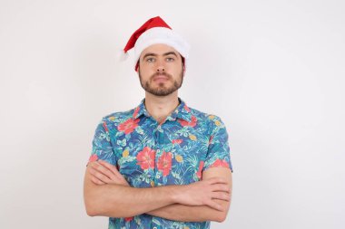 Noel Baba şapkalı genç adam kollarını kavuşturup kameraya bakıyor. Pozitif kişi.