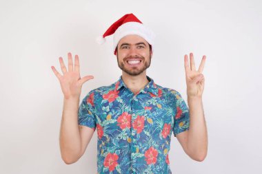 Noel Baba şapkalı genç adam sekiz numarayı gösterip işaret ederken kendinden emin ve mutlu bir şekilde gülümsüyor..