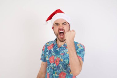 Noel Baba şapkalı genç adam öfkeyle bağırırken yumruk kaldırıyor ve sinirleniyor. Öfke ve agresif kavram.