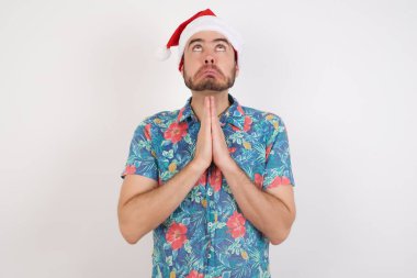 Noel Baba şapkalı genç adam elleri bağlı yalvarıyor ve dua ediyor. Yüzünde umut ifadesi var. Çok duygusal ve endişeli. Soruyorum.