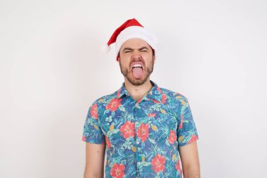 Noel Baba şapkalı genç adam komik bir ifadeyle dilini dışarı çıkarıyor. Duygu kavramı.