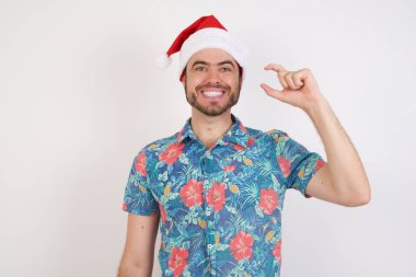 Noel Baba şapkalı genç adam gülümsüyor ve el hareketleriyle hareket ediyor. Küçük boy işareti yapıyor, parmaklarına bakıyor ve kameraya bakıyor. Ölçü kavramı