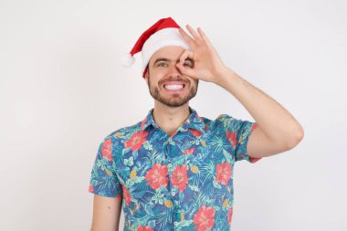 Noel Baba şapkalı genç adam el hareketleriyle gülümsüyor, gözleriyle mutlu yüzüyle parmaklarının arasından bakıyor..