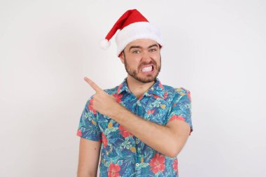 Noel Baba şapkalı genç adam endişeli ve endişeli bir şekilde işaret ediyor..