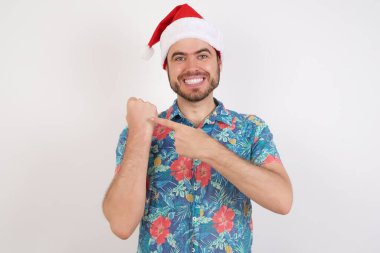 Noel Baba şapkalı genç adam kol saatini işaret ediyor, sabırsız, rahat bir ifadeyle kameraya bakıyor.