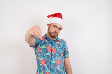 Noel Baba şapkalı genç adam beyaz duvara ciddi ciddi bakıyor.