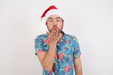 Noel Baba şapkalı genç adam kameraya bakıyor ve havada bir öpücük savuruyor. Güzel ve seksi. Aşk ifadesi.