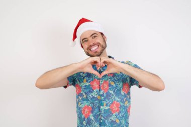Noel Baba şapkalı genç adam elleriyle kalp sembolü yapıyor. Romantik konsept.