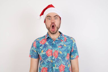Noel Baba şapkalı genç adam şok olmuş bir ifadeyle kameraya bakıyor ve beklenmedik bir şekilde haykırıyor.,