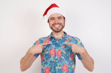 Noel Baba şapkalı genç adamın yatay görüntüsü vücudunu gösteriyor. Alışverişe gidip başarılı alışverişler yaptıktan sonra keyfi yerinde.